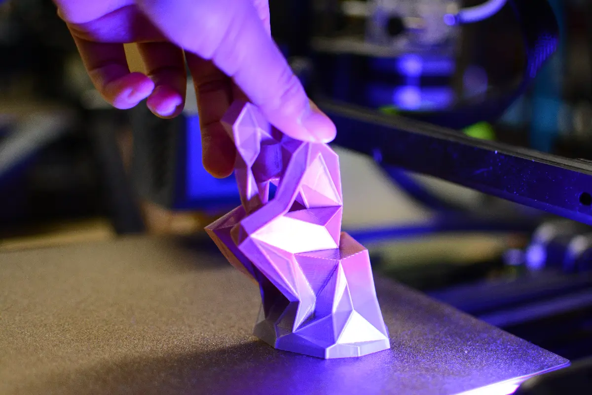 Hand removing a 3D-printed geometric sculpture from a printer. Creative industry co-op placement project.