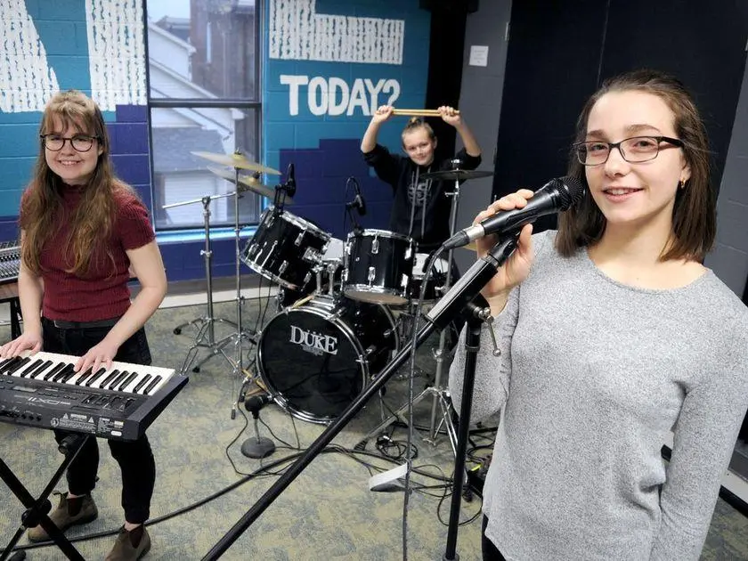 Three young women in a music studio during a co-op placement, playing keyboards and drums.